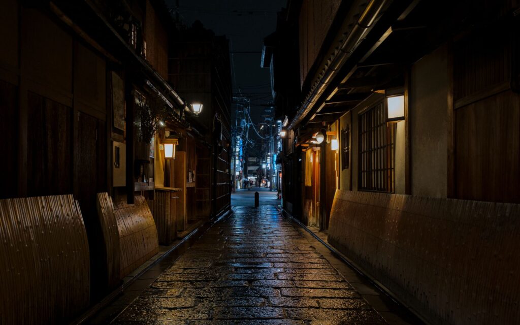A lantern-lit stone alley lined with wooden machiya at night in Gion, Kyoto