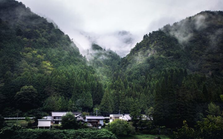 Small village beneath misty forested mountains in rural Japan