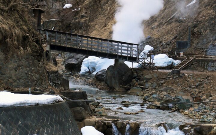 Steam rising from a hot spring beside a snowy mountain stream in Japan