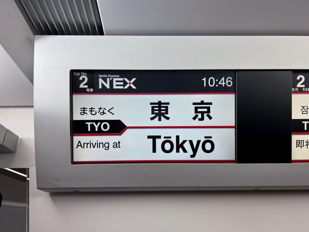 An in-train display on the Narita Express showing arrival at Tokyo Station in Japanese and English