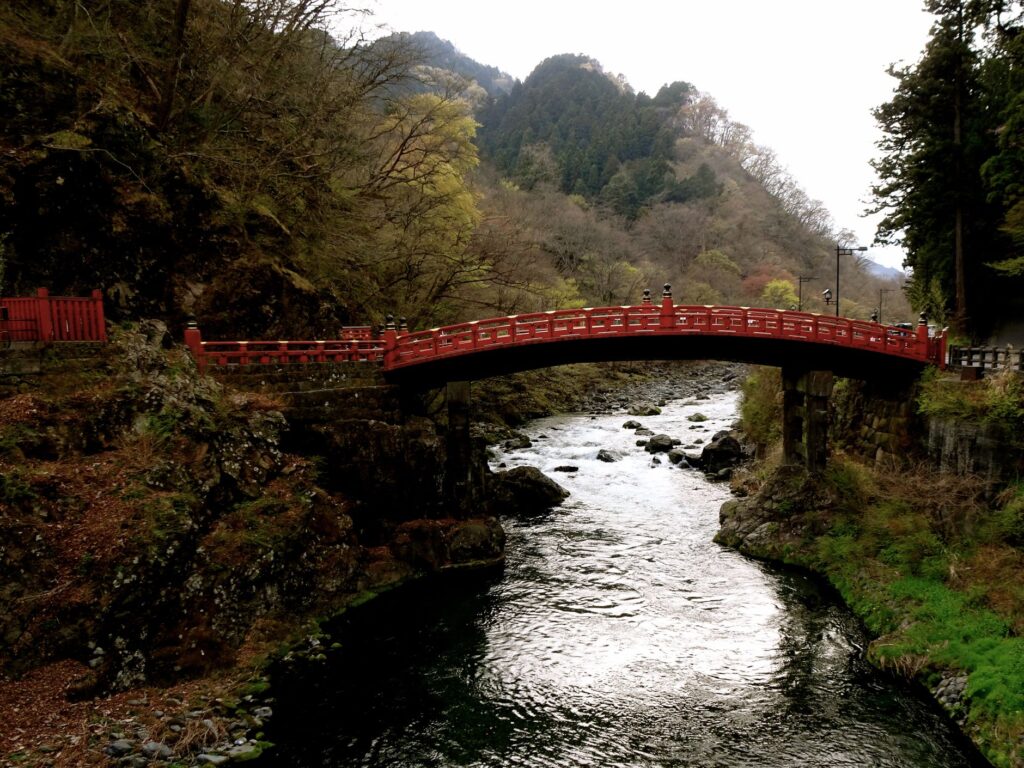 The red Shinkyo Bridge over the Daiya River surrounded by green forest in Nikko