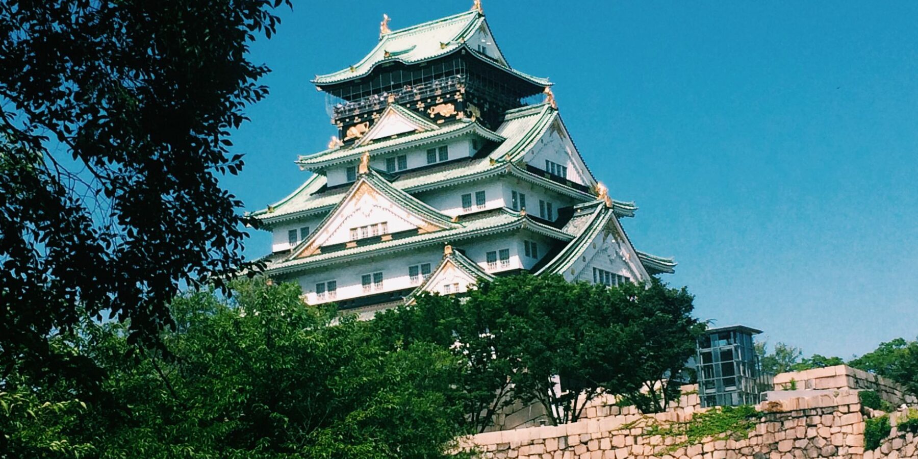 Osaka Castle main keep above stone walls and trees under a blue sky, Osaka, Japan