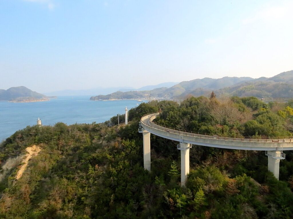 A curving bicycle ramp climbing toward a Shimanami Kaido bridge