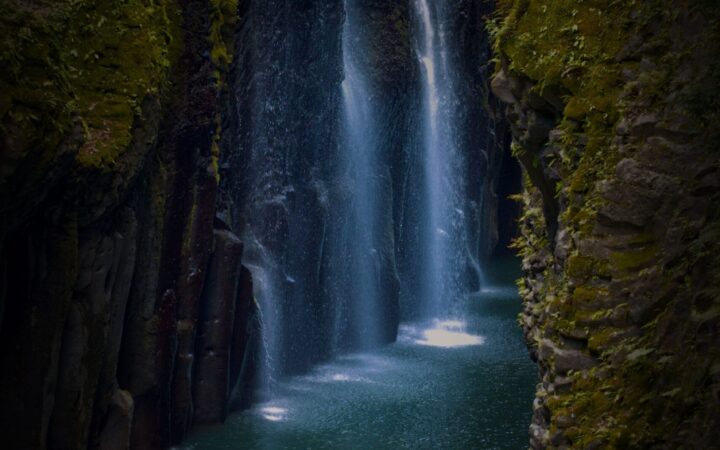Manai Falls pouring into Takachiho Gorge with a rowboat on the emerald river, Miyazaki